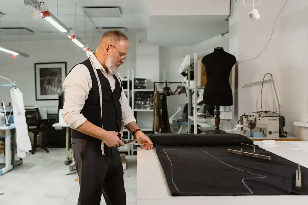 Tailor meticulously cutting fabric on a wooden drafting table